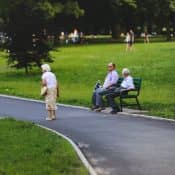 Una anciana pasa junto a dos personas sentadas en un banco de un parque