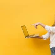 femme pointant du doigt un ordinateur portable qu'elle tiens de son autre main sur fond jaune