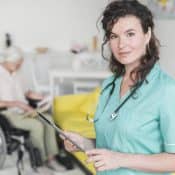 portrait de femme en tenue d'infirmière tenant un bloc notes avec une personne en fauteuil roulant en arrière plan
