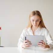 jeune femme blonde assise à un bureau lisant sur une tablette