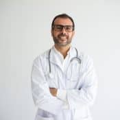 un médecin en blouse blanche pose les bras croisés sur un fond blanc