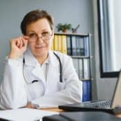 femme médecin tient ses lunettes devant son ordinateur portable