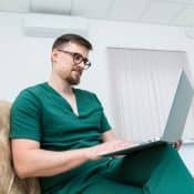 Médecin portant une blouse d'hôpital assis sur un canapé, un ordinateur portable sur les genoux