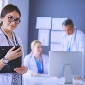 femme docteur avec un stéthoscope et un bloc notes debout devant deux autres médecins autour d'un bureau