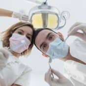Deux dentistes se penchant sur un patient, munis de masques et d'instrucments médicaux
