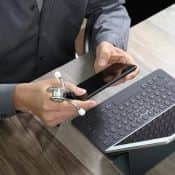 Homme assis à un bureau avec un stéthoscope et un téléphone dans les mains, un ortinateur portable devant lui